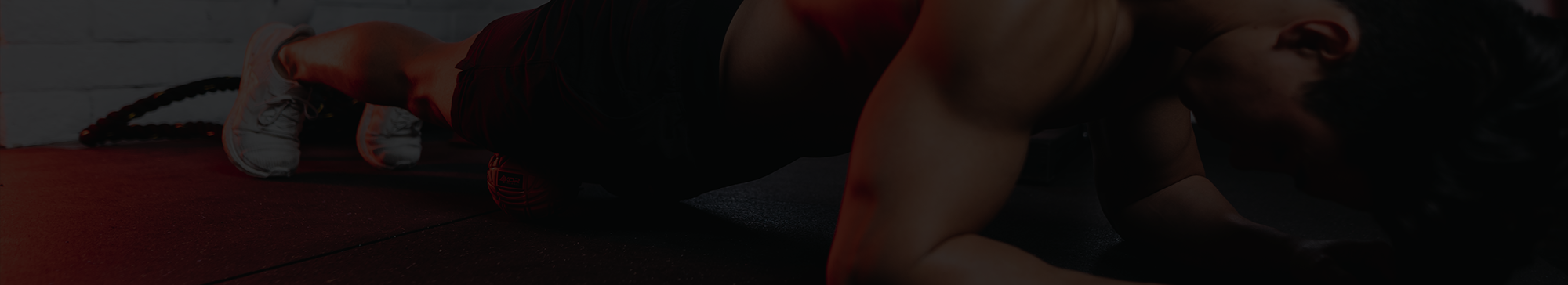 Male athlete lying on gym floor using 4KOR Fitness Fireball massage ball for lower body muscle recovery in a dark gym setting